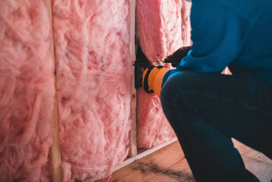 Ouvrier posant de la laine de verre rose entre les montants d'un mur